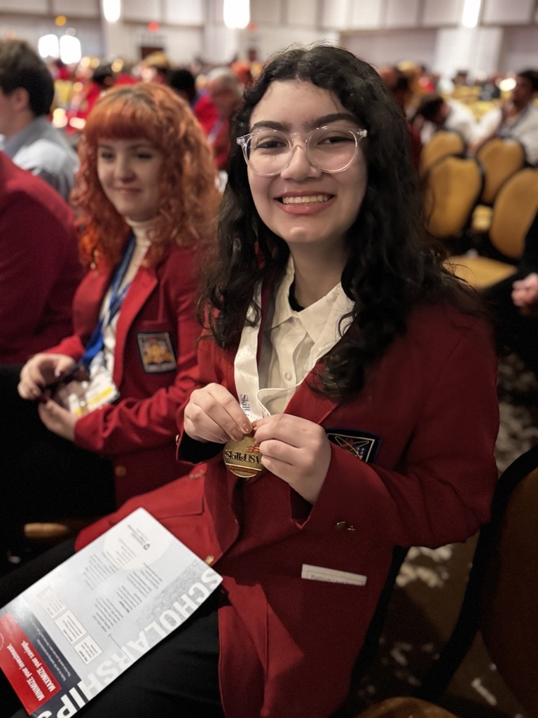 A BCTC student in a red SkillsUSA blazer smiles while seated and holding her medal, with another student seated beside her at the ceremony.