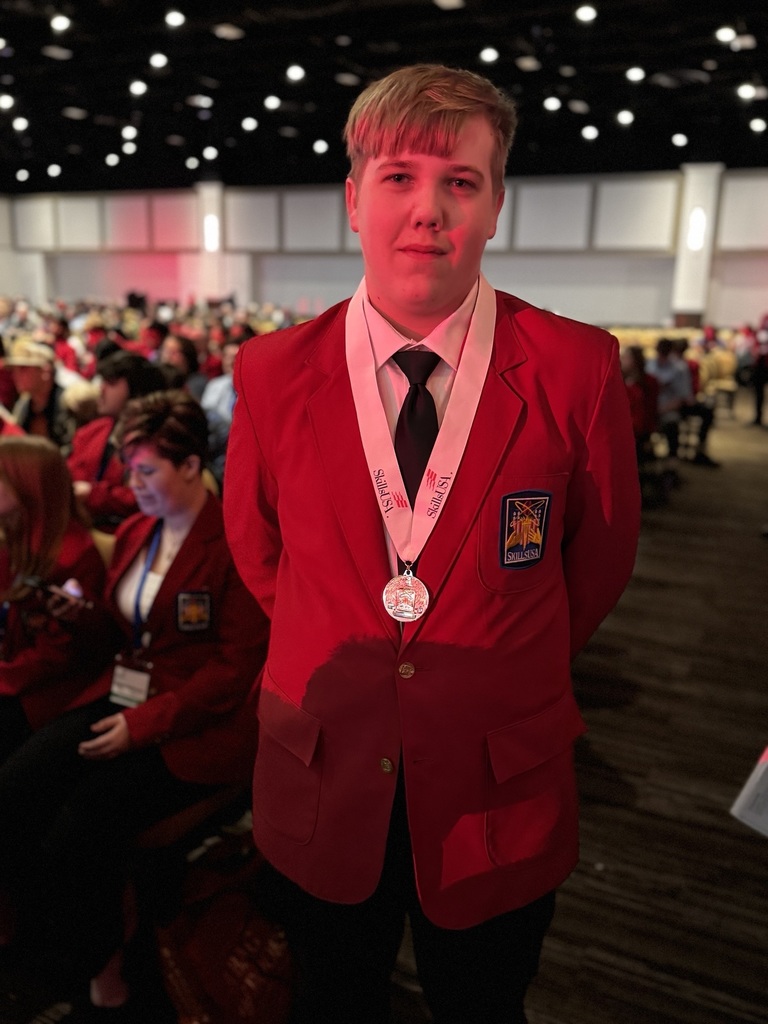 A BCTC student in a red SkillsUSA blazer stands in the auditorium wearing a medal and smiling for a photo, with the awards crowd visible behind him.