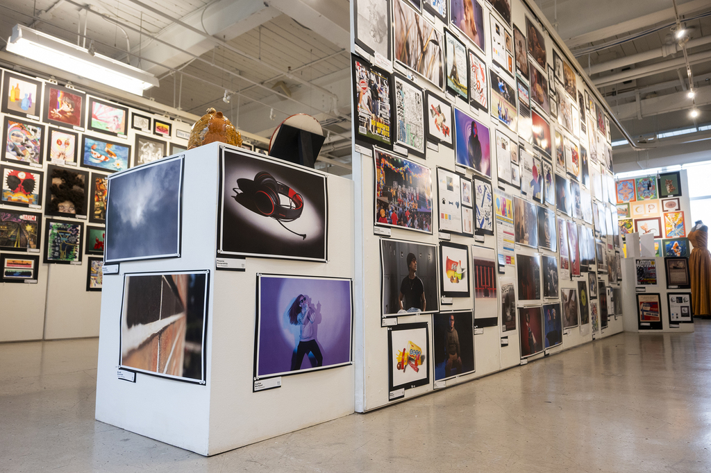 Angled view of a gallery corner displaying student photography and digital artwork mounted on white walls.