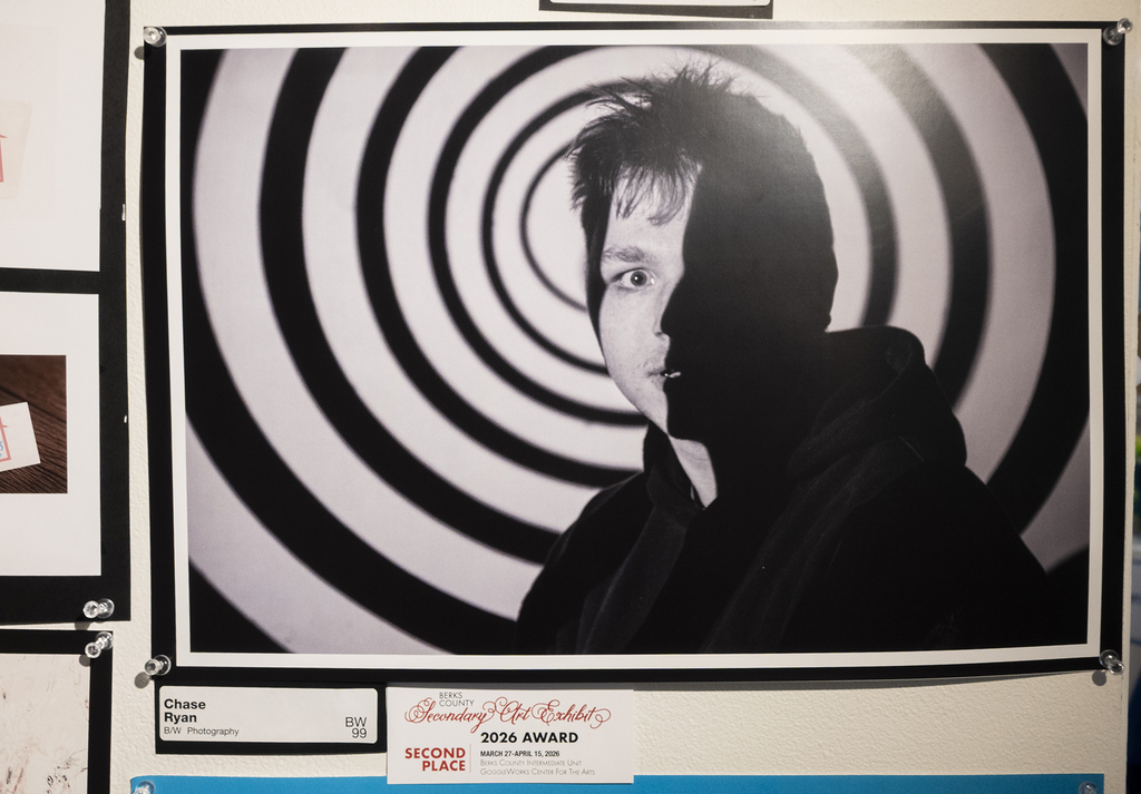 Black and white portrait of a person with dramatic lighting and a spiral pattern background, displayed in the exhibit.