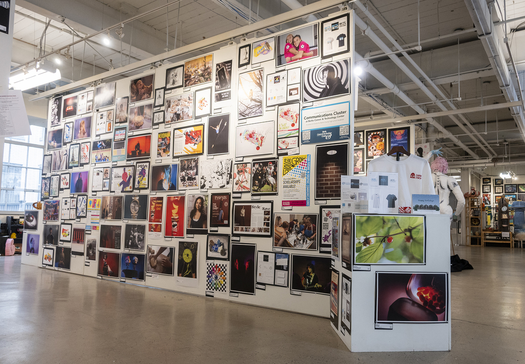 Wide view of a gallery display wall featuring dozens of student photographs and designs arranged in a grid.