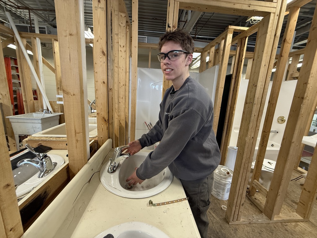 Student installs a faucet and drain in a sink set into a countertop in a plumbing lab.