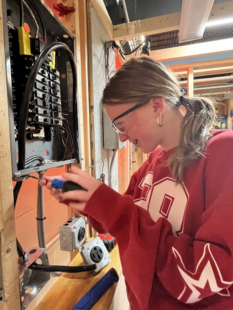 Students strip wires and make electrical connections inside a box.