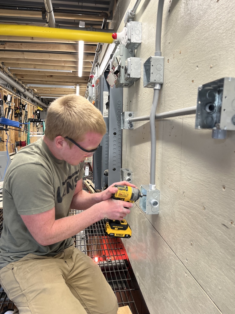 Student uses a drill to fasten conduit and boxes to a training wall.