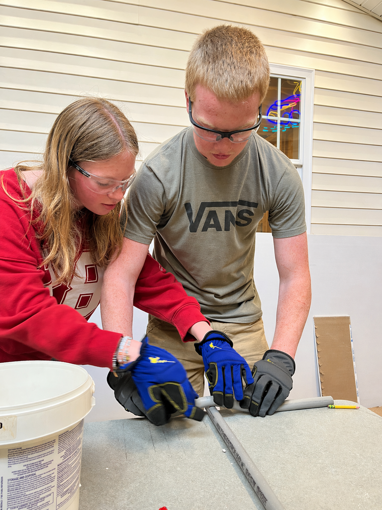 Students bend and cool heated PVC conduit at a workbench in an electrical lab.