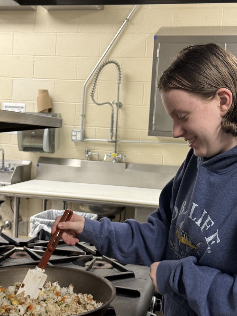Student smiles while stirring fried rice in a skillet on a commercial stove.