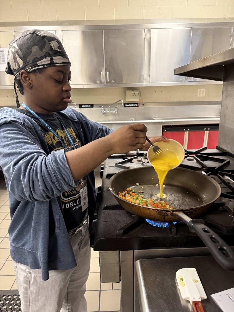 Student pours beaten eggs into a skillet with mixed vegetables over a lit burner.