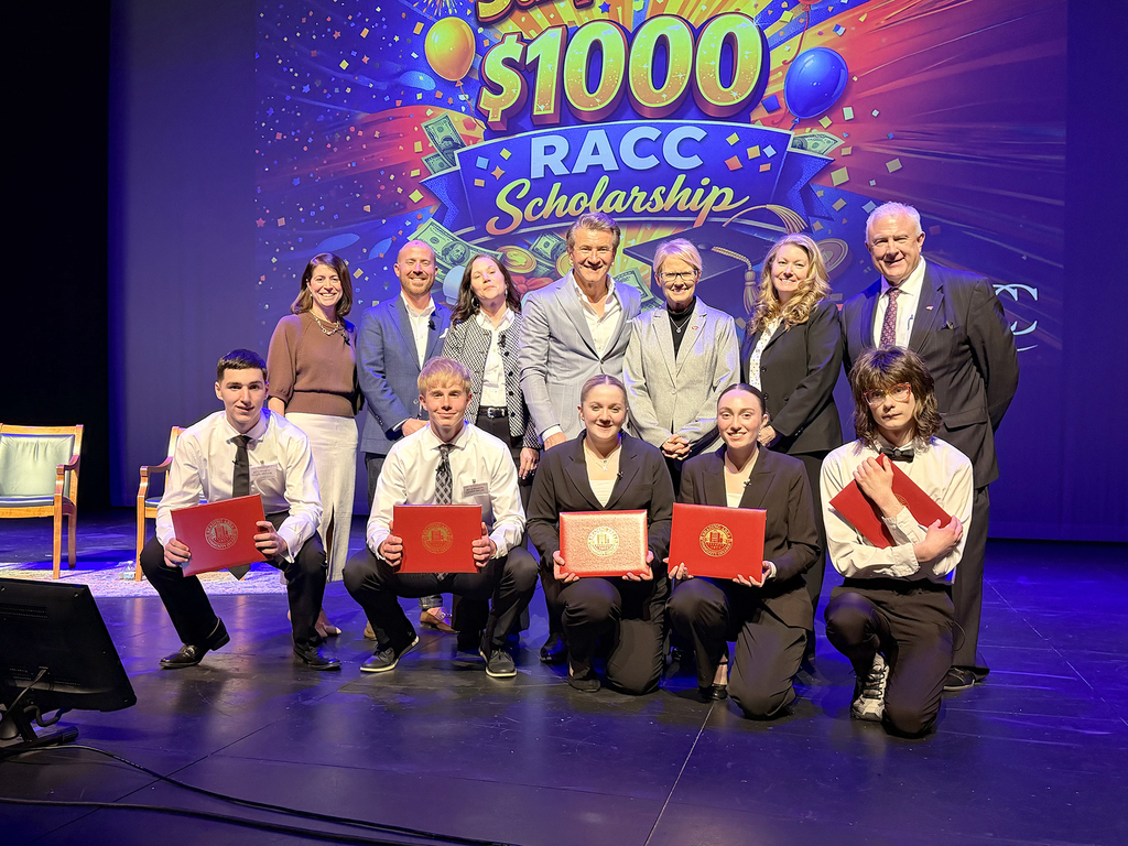 BCTC students kneel on stage holding scholarship certificates with Robert Herjavec and event organizers behind them.