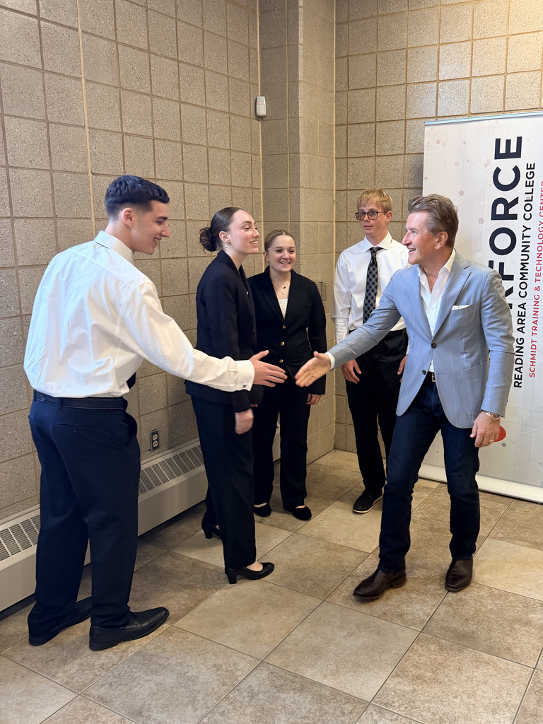 Robert Herjavec speaks with BCTC students in business attire in a hallway at Reading Area Community College.