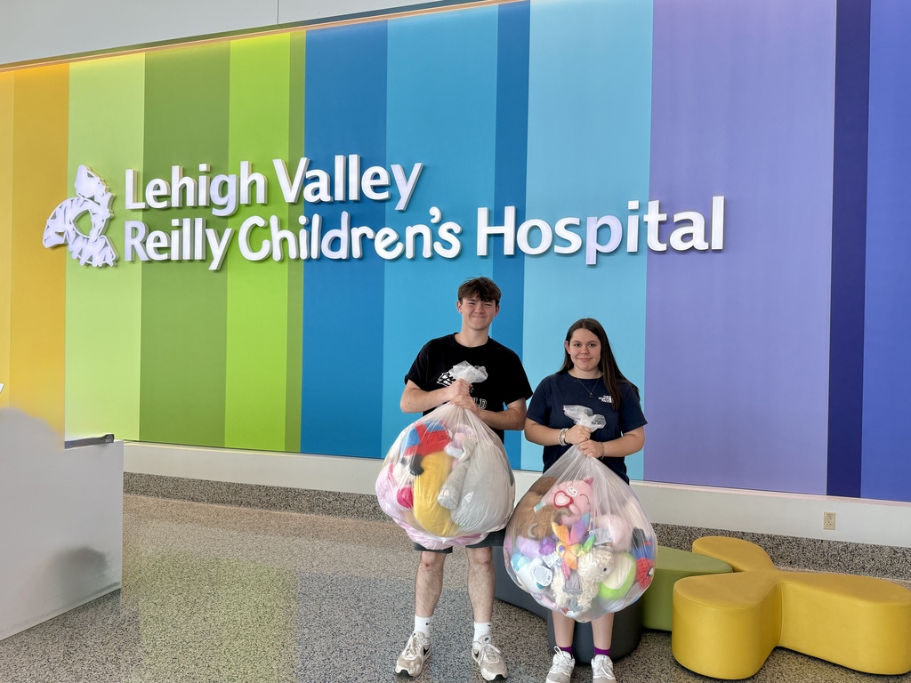 Two students stand inside Lehigh Valley Reilly Children’s Hospital holding large bags filled with donated stuffed animals against a colorful wall backdrop.