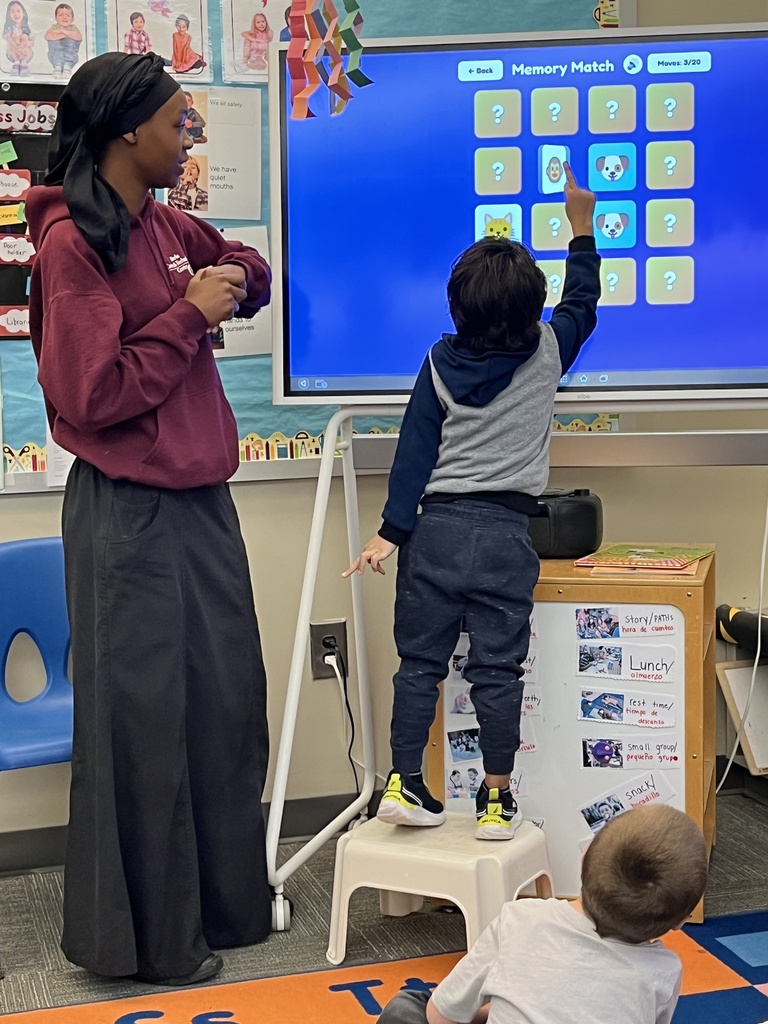 A young learner plays a memory matching game on a smartboard while a BCTC student stands nearby.
