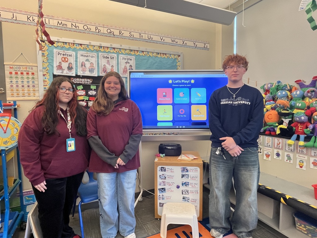 Three BCTC students stand in an Early Childhood Education classroom beside a smartboard displaying student-created games.