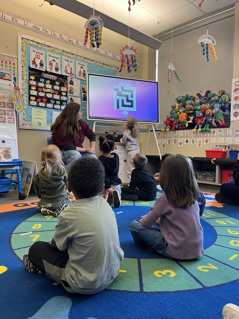 Young learners sit on a classroom rug while a BCTC student leads an interactive game on a smartboard.