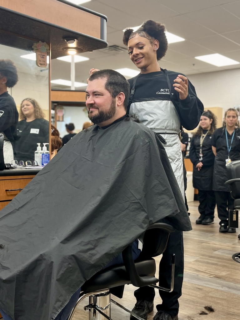 Cosmetology student stands behind Mr. Entrekin after using clippers to shave part of his hair.