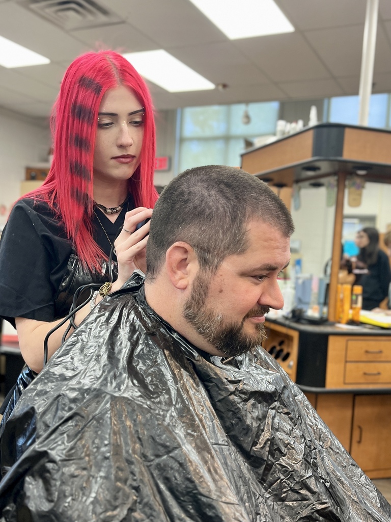 Cosmetology student with bright pink hair uses clippers to trim Mr. Entrekin’s hair in the student salon.