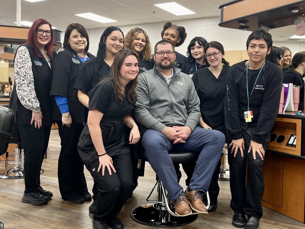 Cosmetology instructors and students gather around Mr. Entrekin in the salon after students shaved his head.