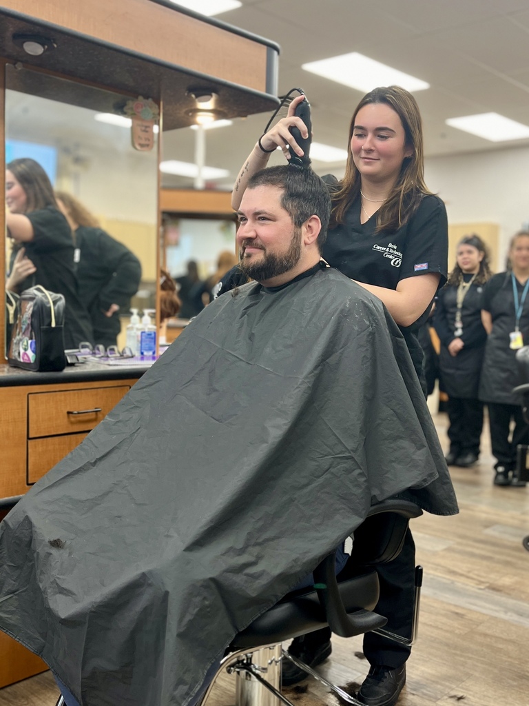 Cosmetology student smiles while using clippers on the top of Mr. Entrekin’s head in the student salon.