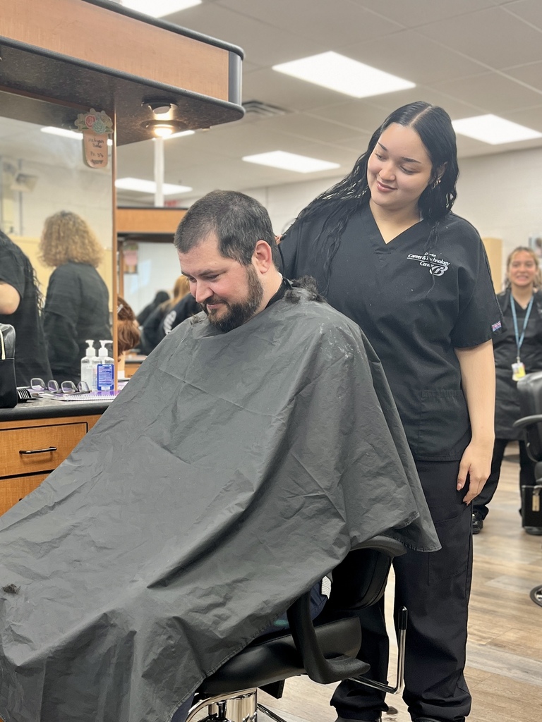 Cosmetology student smiles beside Mr. Entrekin after helping shave his hair in the student salon.