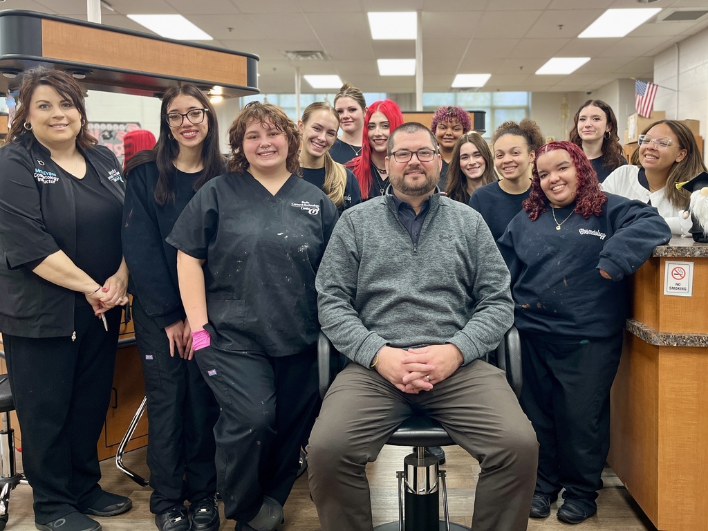 Cosmetology instructors and students gather around Mr. Entrekin in the salon after students shaved his head.