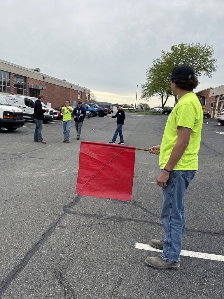 A student holds a red flag while classmates practice traffic control procedures during PennDOT Flagger Certification training.