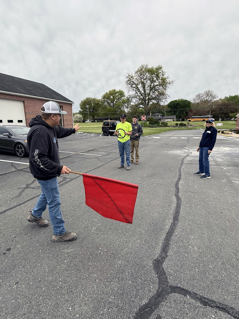A student uses a red flag to direct classmates during a work zone safety training exercise.