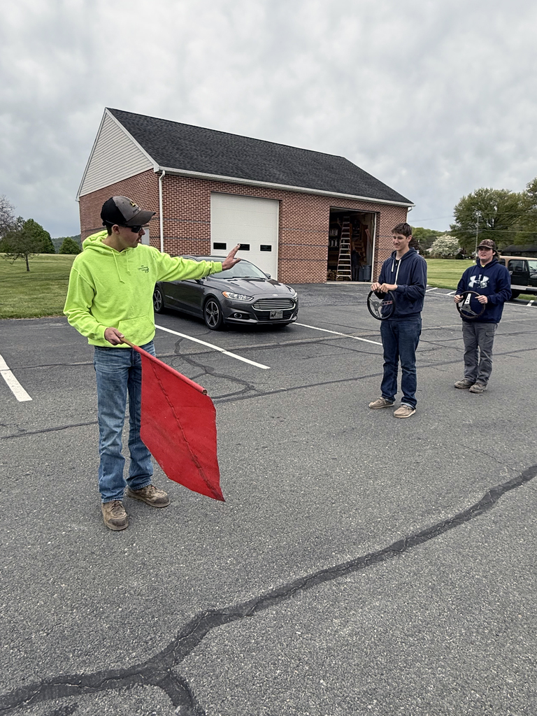 A student demonstrates a stop signal with a red flag while classmates observe during flagger training.