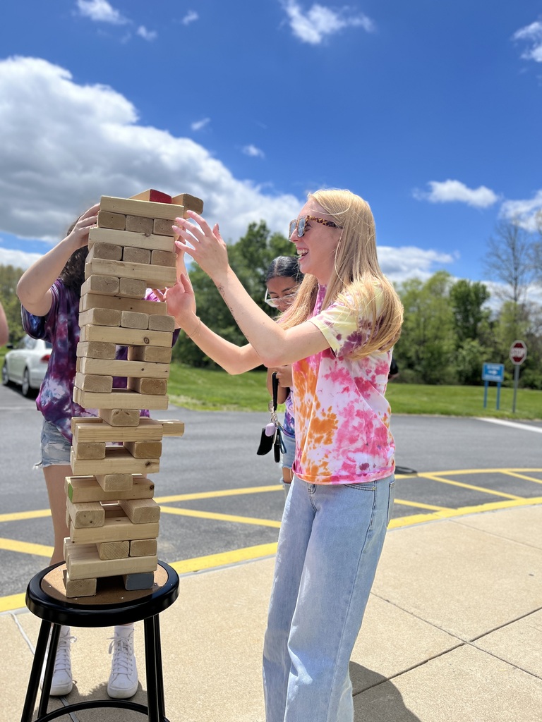 Student laughs while playing a giant wooden block stacking game outside.