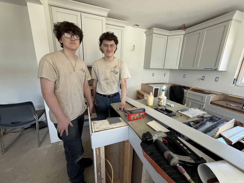 Two Cabinetry & Wood Technology students stand beside a custom island and installed cabinets in the Student-Built House kitchen.