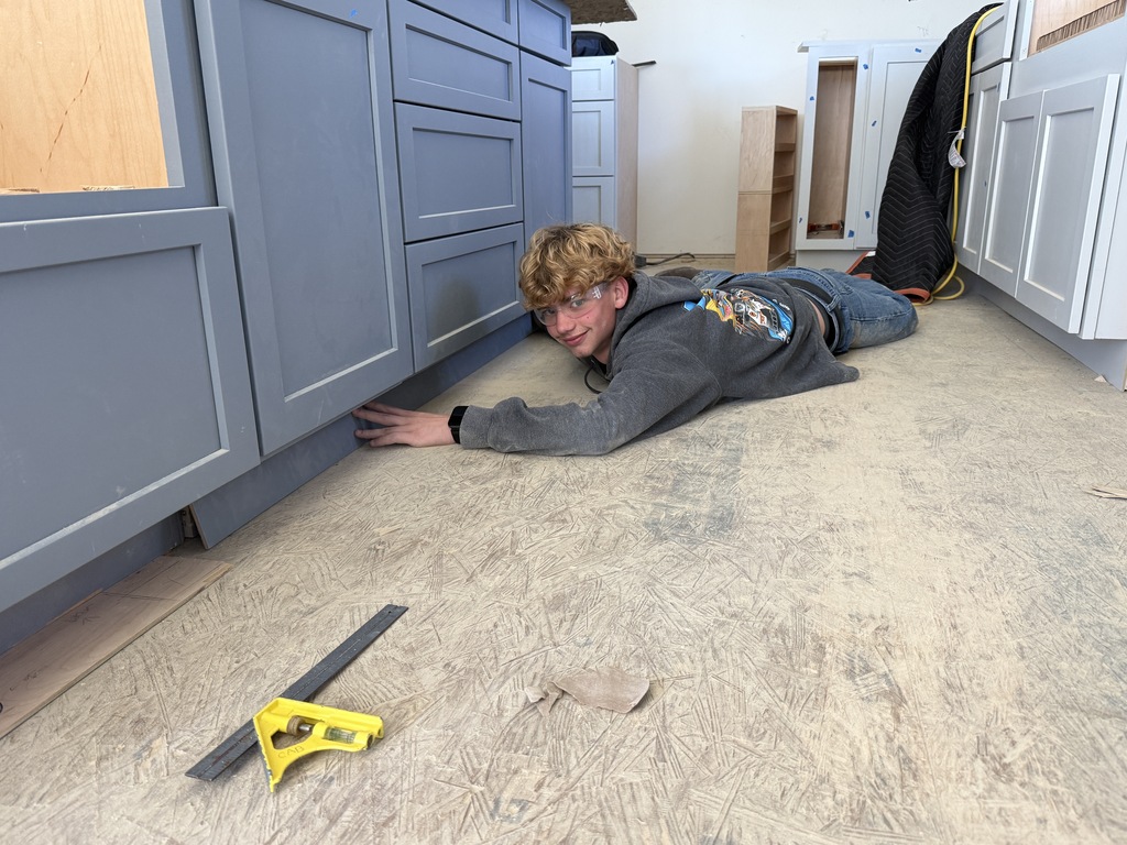 A Cabinetry & Wood Technology student lies on the floor while adjusting the base of installed kitchen cabinets.