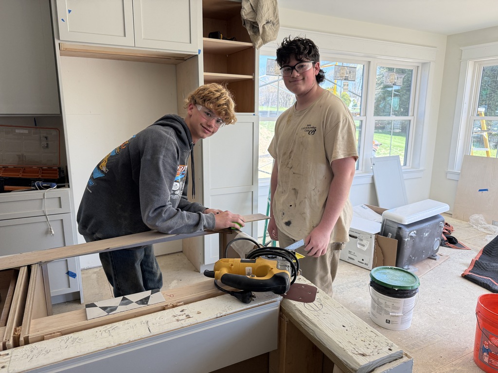 Two Cabinetry & Wood Technology students work near a custom kitchen island inside the Student-Built House.