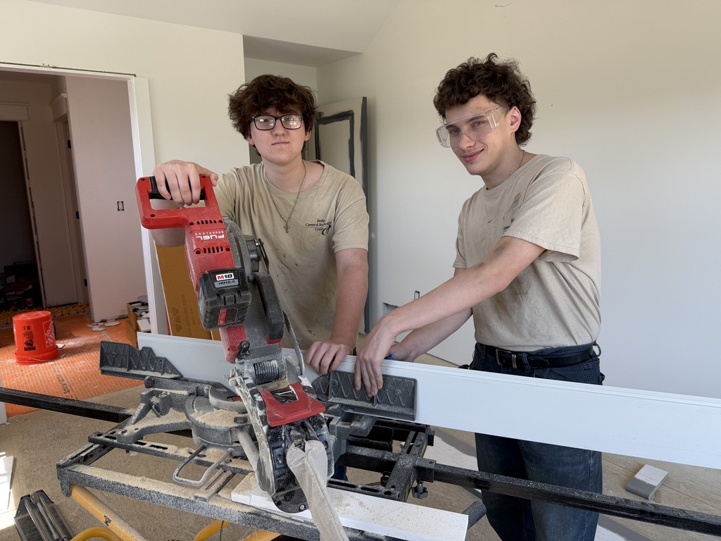 Two Cabinetry & Wood Technology students stand behind a miter saw while working on trim for the Student-Built House kitchen.