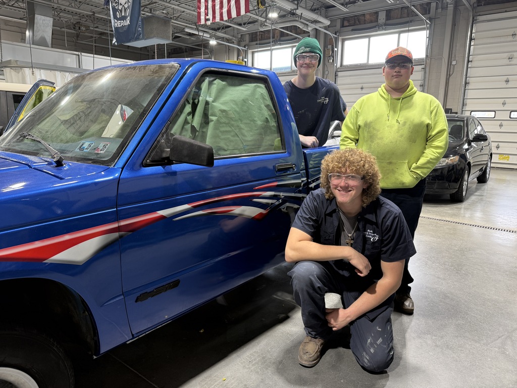 Three Automotive Collision Repair Technology students pose beside a blue truck with red, white, and blue decals in the auto shop.