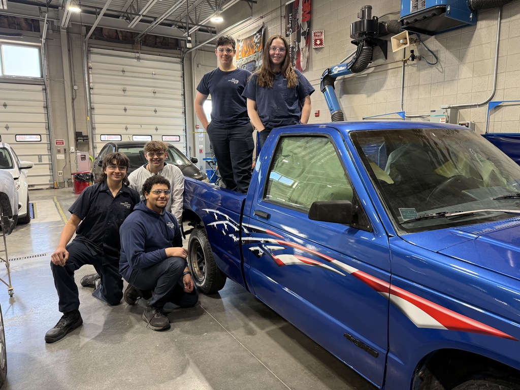 Six Automotive Collision Repair Technology students pose around a blue truck with patriotic decals in the auto shop.