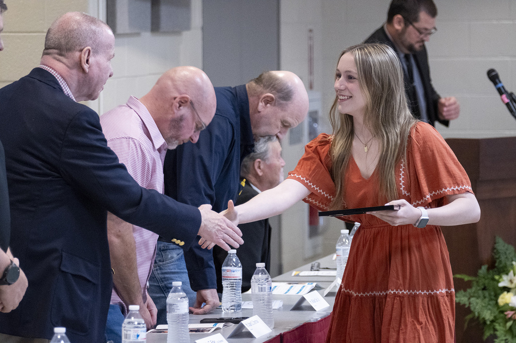 A BCTC student smiles while shaking hands with school representatives and holding an award certificate.