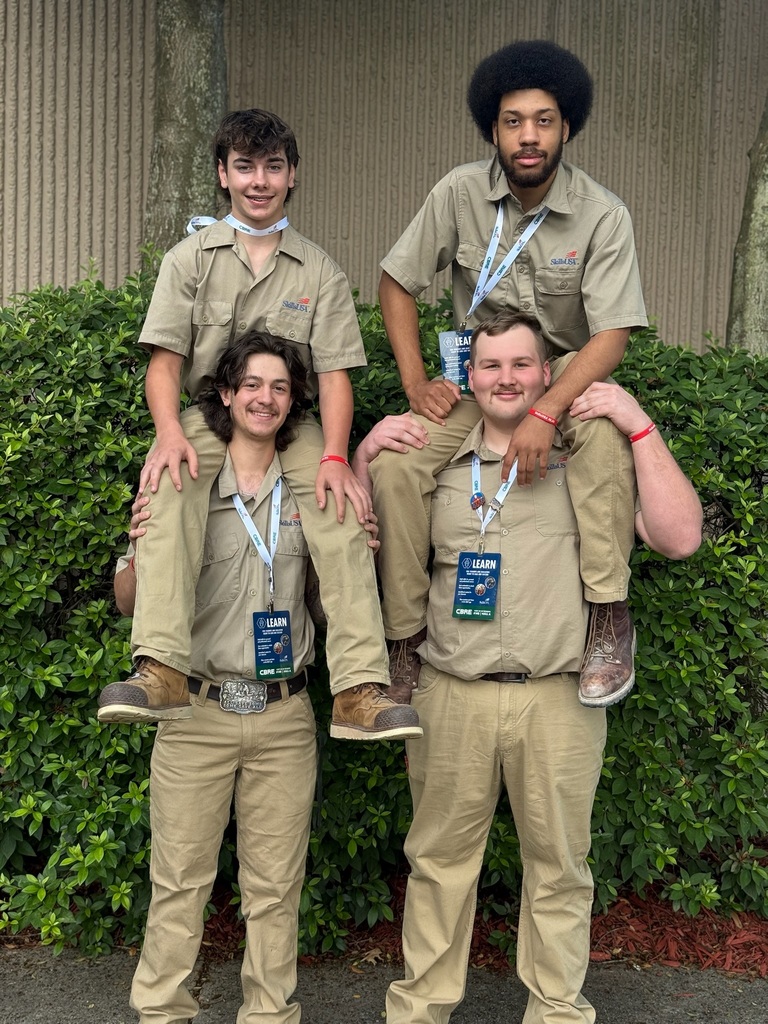 Four BCTC students wearing SkillsUSA uniforms pose together outside near shrubs during the national conference in Atlanta.