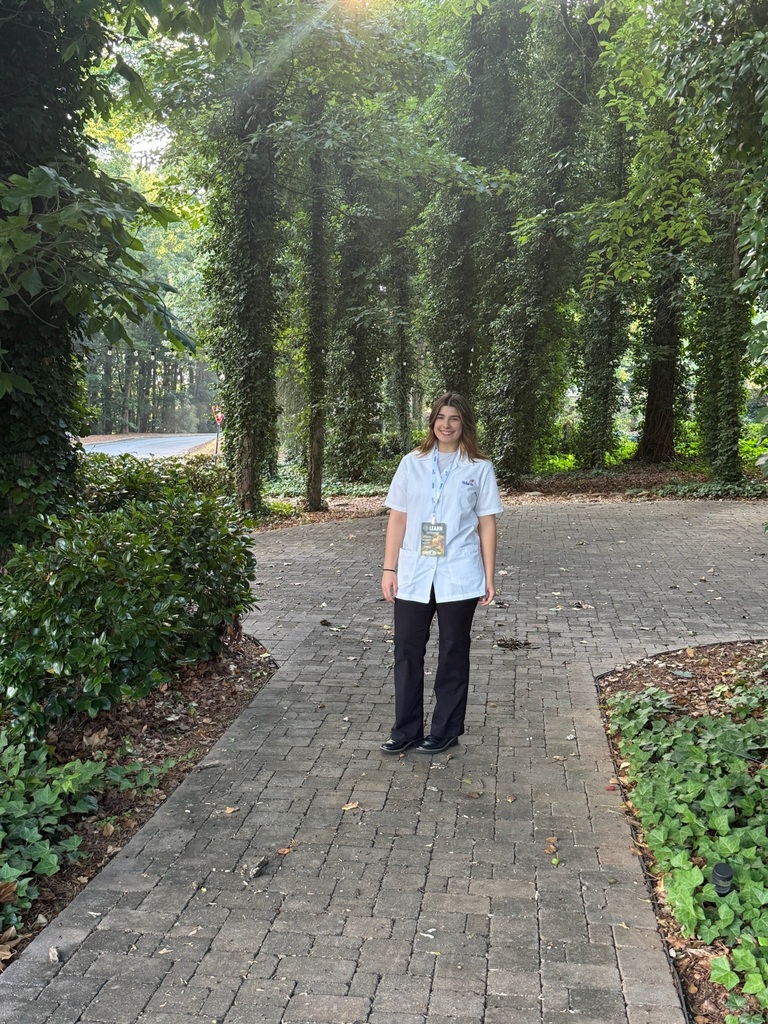 A BCTC student wearing a SkillsUSA uniform poses outside on a walkway surrounded by trees and greenery.
