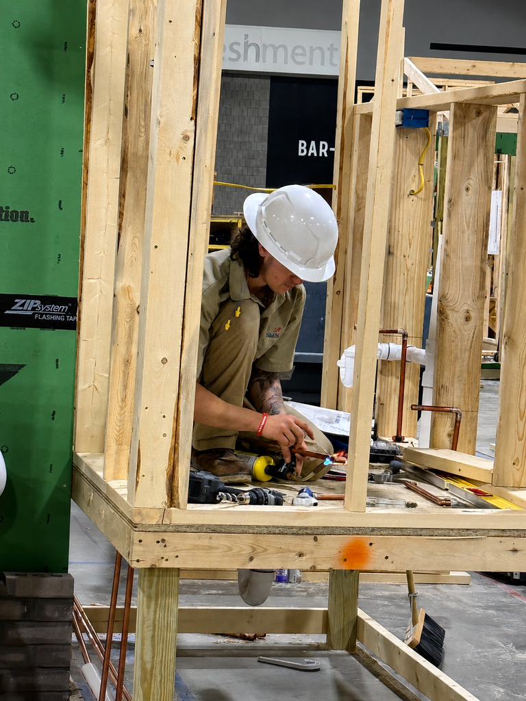 A BCTC competitor solders copper pipe inside a framed structure.