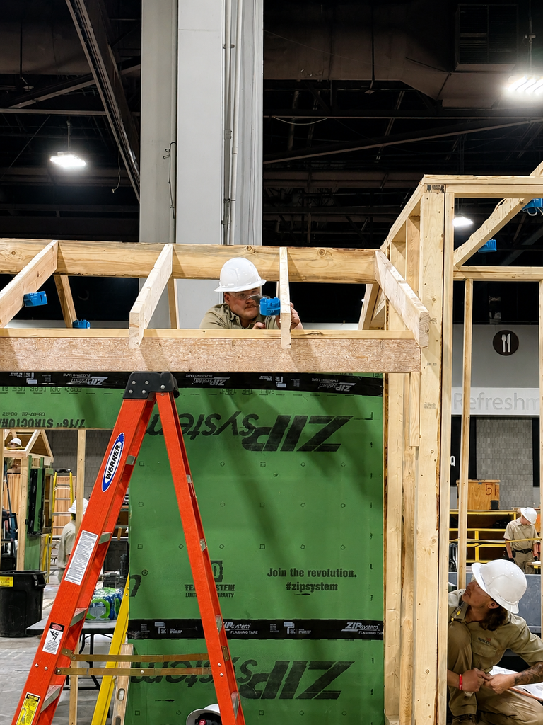 A construction competitor works on a framed wall while wearing a hard hat.