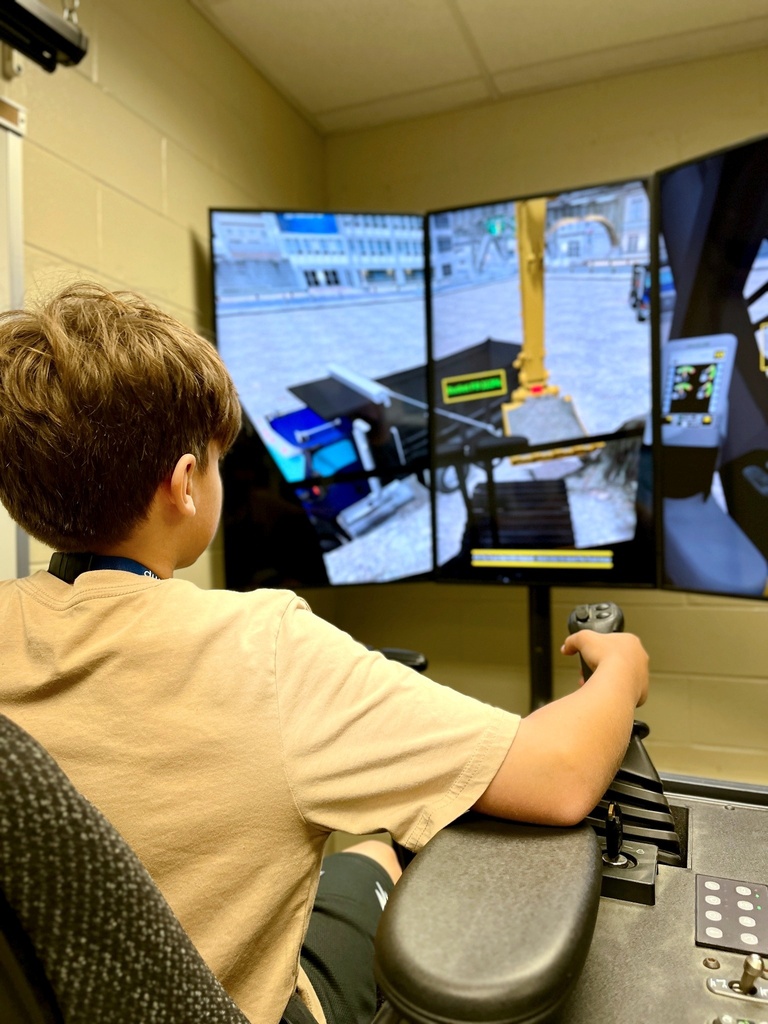 A Career Camp participant uses a heavy equipment simulator with multiple screens and hand controls.