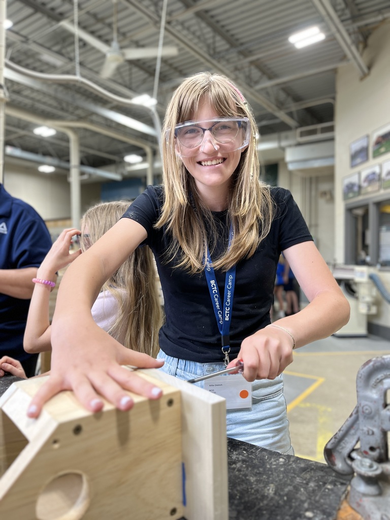 A smiling Career Camp participant uses a screwdriver while working on a wooden birdhouse project.