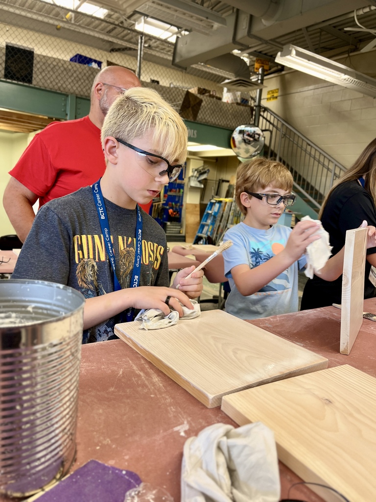 Career Camp participants wearing safety glasses apply finish to wooden boards in a BCTC woodworking lab.