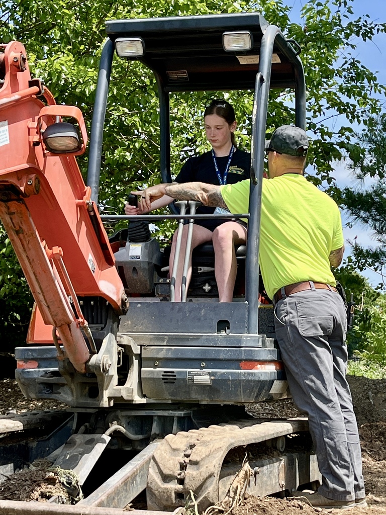 A Career Camp participant sits in the operator seat of an excavator while an instructor provides guidance.