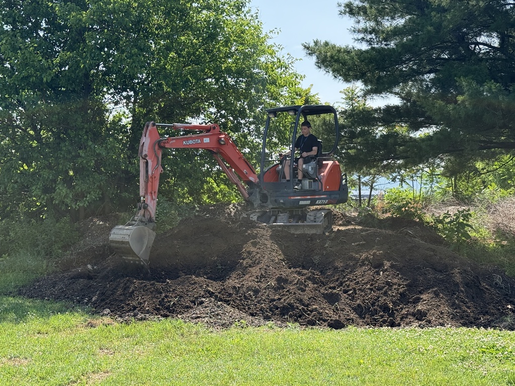 Career Camp participant operates a small excavator outdoors during a heavy equipment activity.