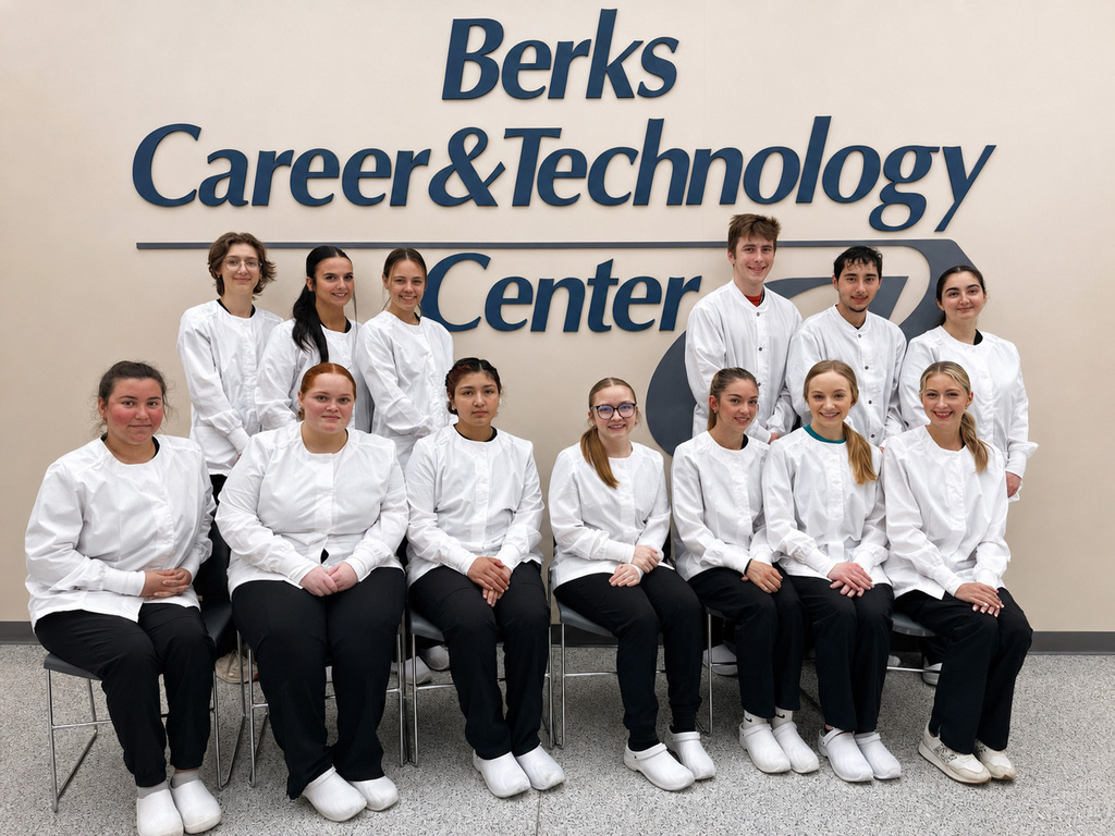 Dental Occupations seniors wearing white lab jackets pose for a group photo in front of the Berks Career & Technology Center wall sign.