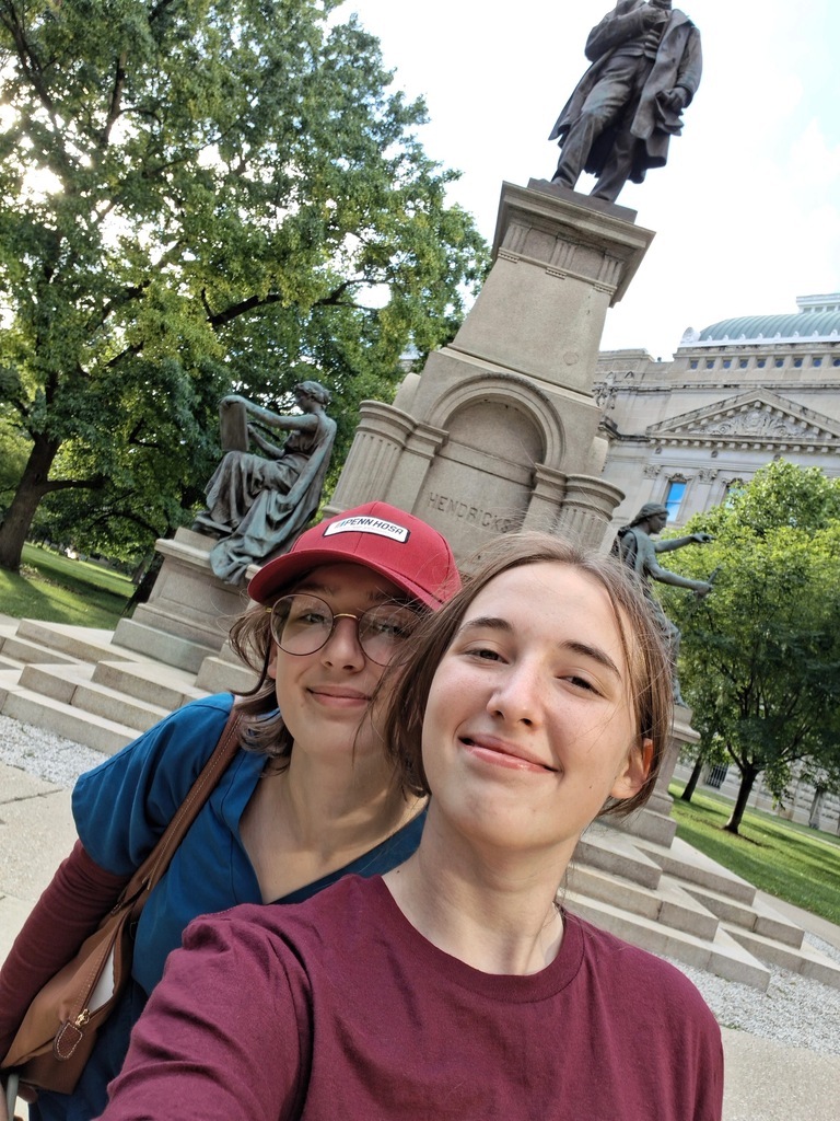Two BCTC HOSA students take a selfie in front of a statue and green trees in Indianapolis.
