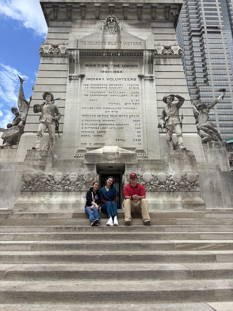 Three BCTC HOSA students sit on the steps of a large stone monument in Indianapolis.