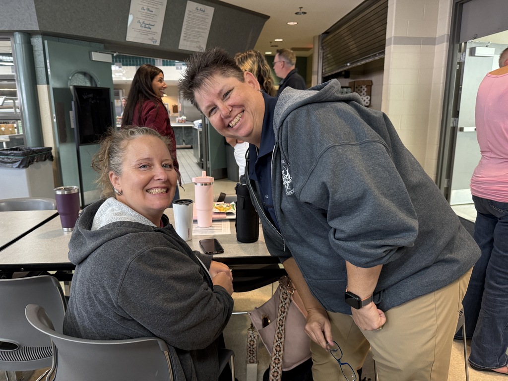 Two women smiling and posing for a photo. One wears a gray hoodie, and the other wears a gray hoodie with a blue shirt underneath.