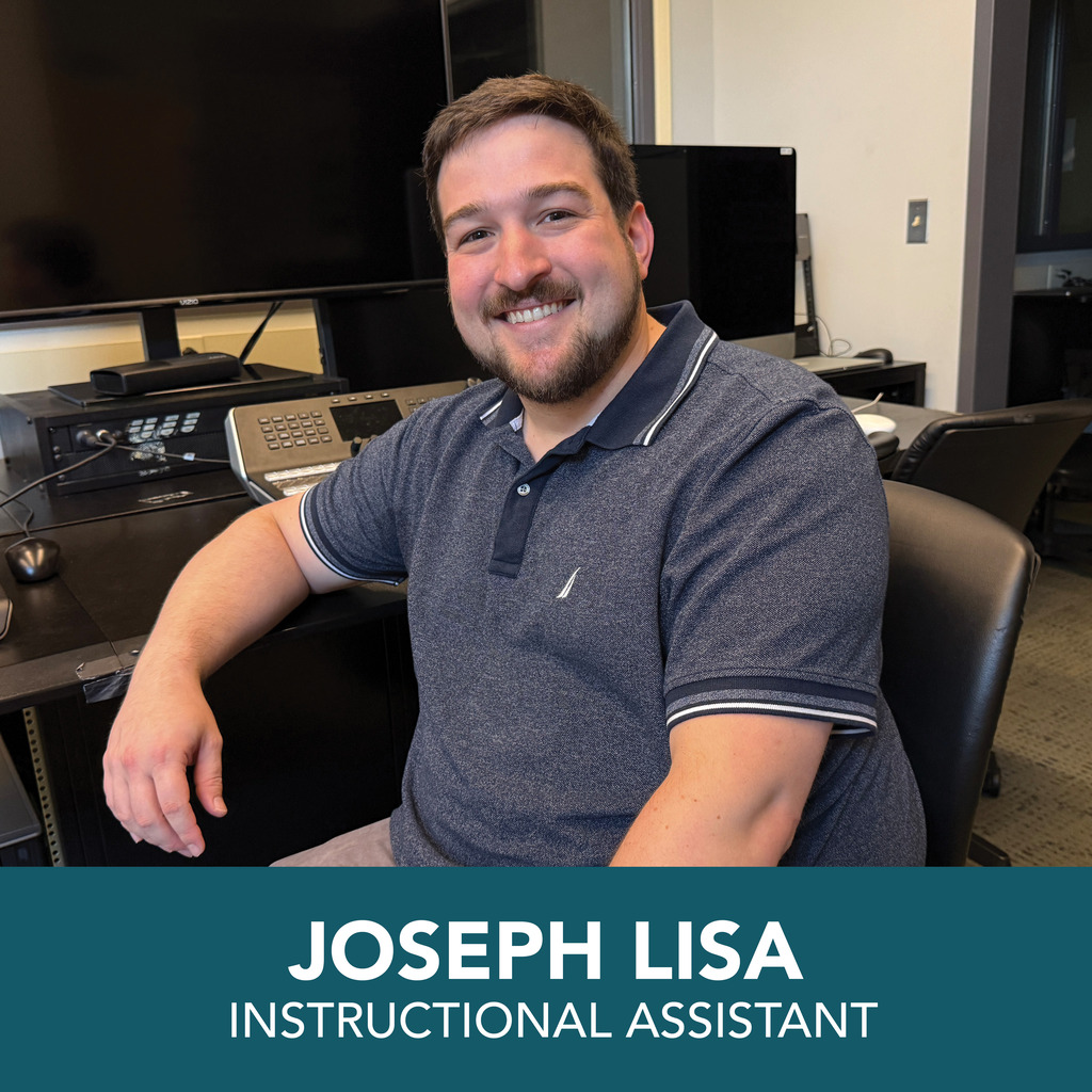 A man, Joseph Lisa, sits at a desk with a microphone. He wears a gray polo shirt. Behind him is a monitor, keyboard, and mouse.