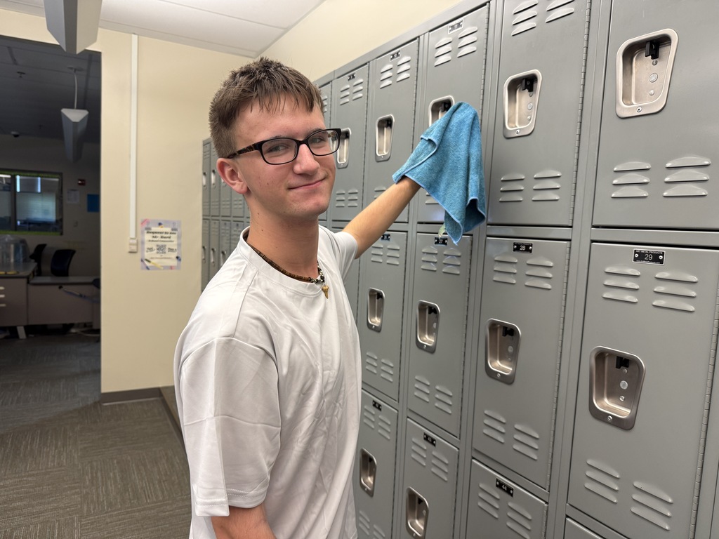 A person in a white shirt and glasses cleans a locker with a blue cloth.