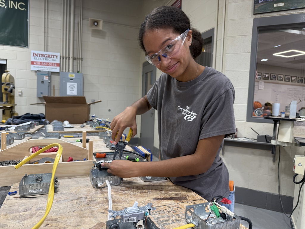 Woman wearing glasses and a gray shirt working on a project in a workshop.